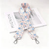 A floral patterned pink and blue nylon strap with a silver metal buckle displayed next to its packaging.