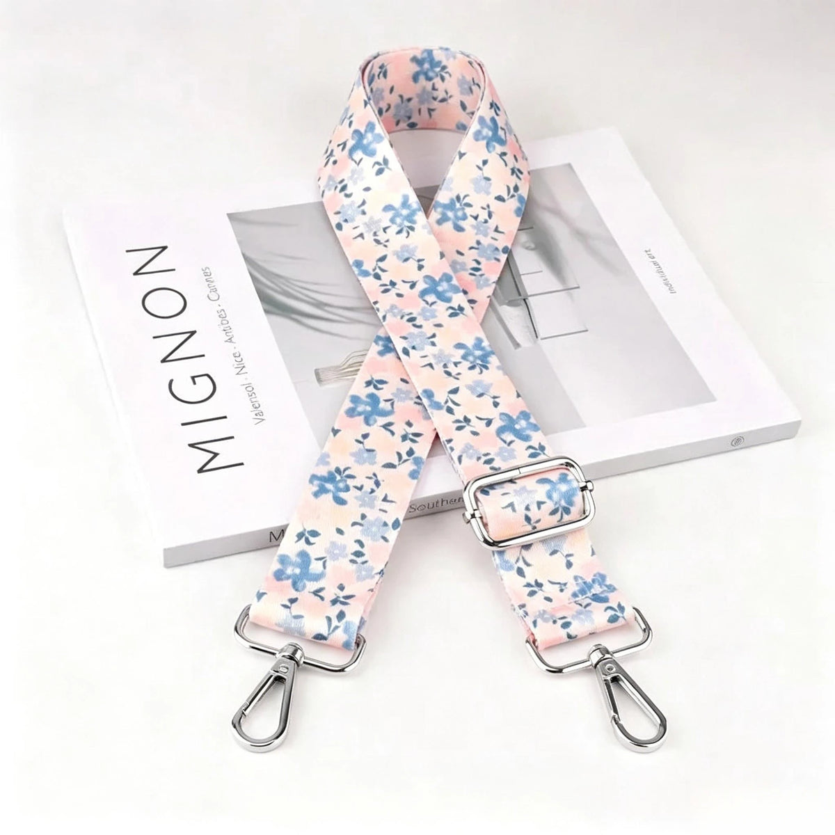 A floral patterned pink and blue nylon strap with a silver metal buckle displayed next to its packaging.