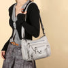 A woman wearing a black sweater and grey top is holding a light silver leather tote bag.