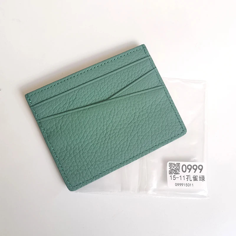 Porte-cartes en cuir véritable bleu sarcelle avec bord surpiqué, dans un emballage plastique transparent.