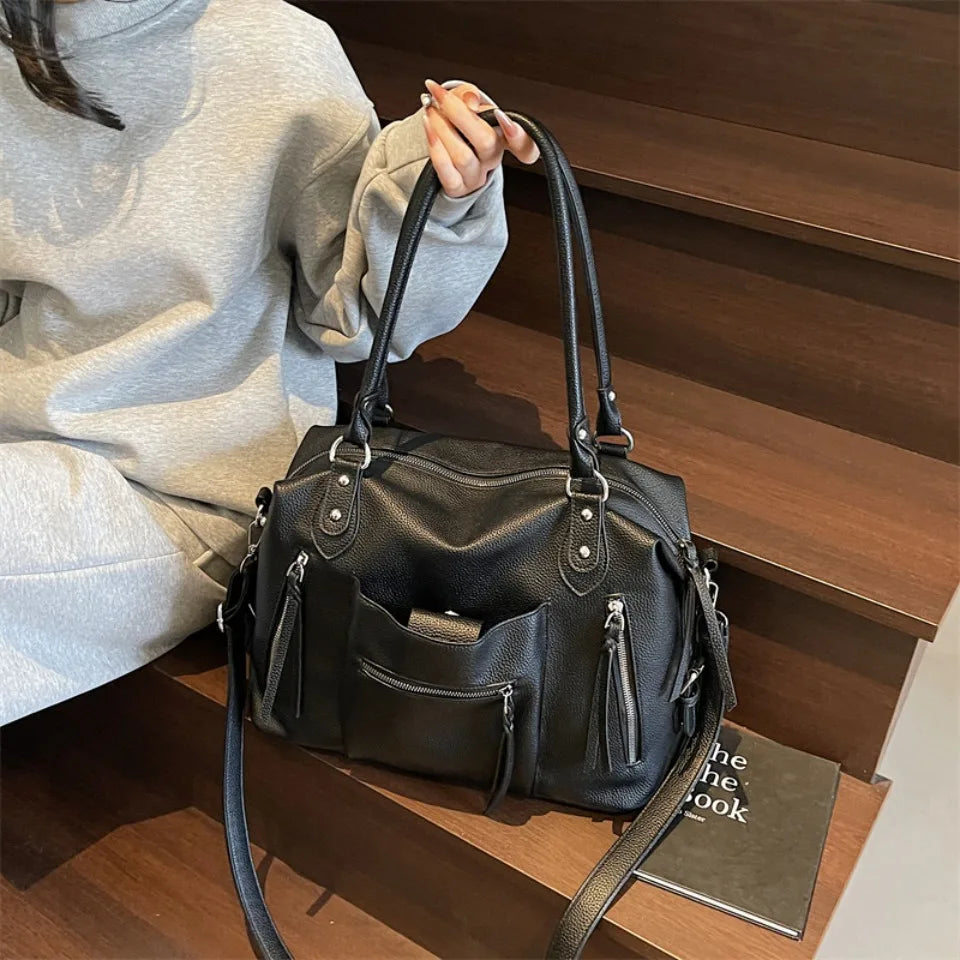 Un bolso cruz de cuero suave negro de lujo sostenido por una persona contra un fondo de madera oscura.