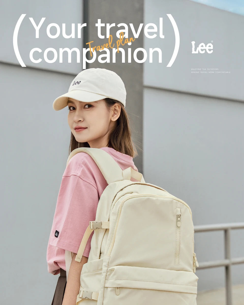 A young woman wearing a pink shirt and a white cap carries a beige Oxford school backpack outdoors.