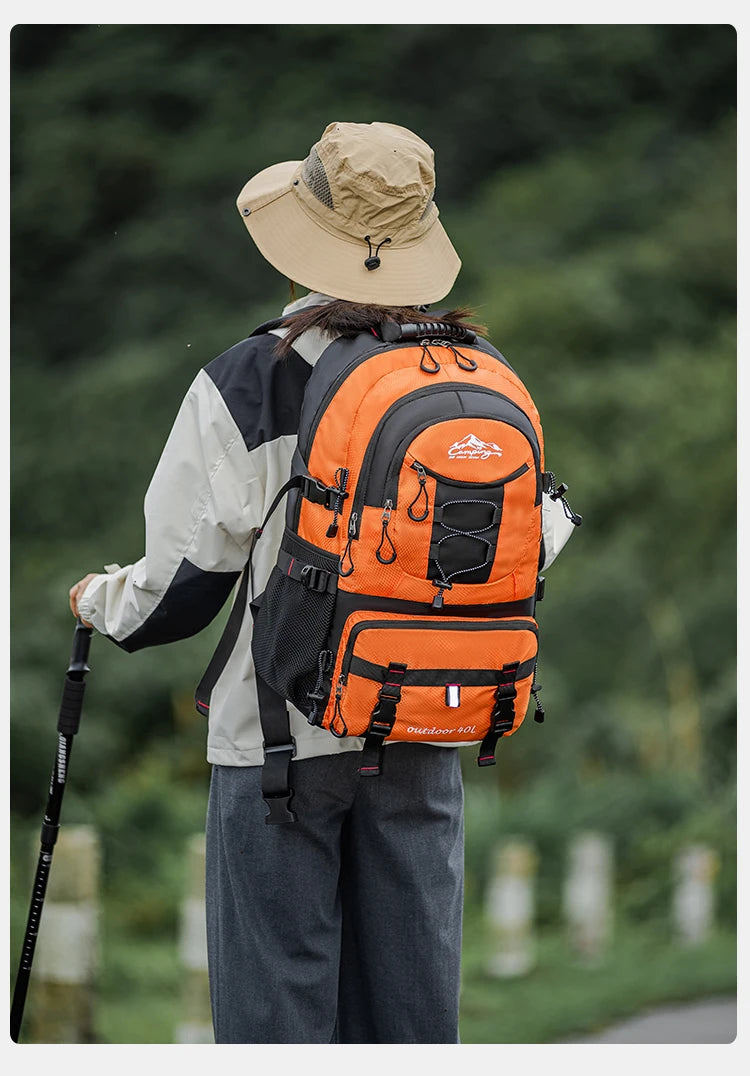 A person wearing a wide-brimmed hat and a large orange hiking backpack is standing outdoors.