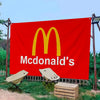 A large red banner featuring the McDonald's golden arches logo and the brand name in white text, set outdoors.