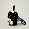 A black cat plush keychain with yellow eyes and a white paw, attached to a black cord.