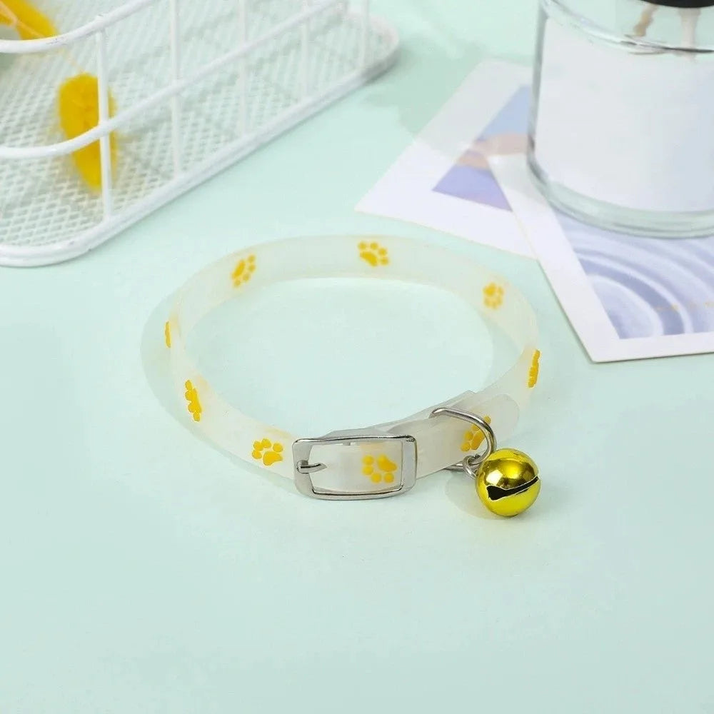 A white glow-in-the-dark pet collar with yellow paw prints is displayed on a light green surface.