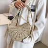 A woman holds a beige handmade rattan straw crossbody bag against a white blazer.