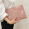 A person holds a pink crocodile print clutch bag against a light beige background.