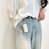 A person wearing a white blouse and light wash jeans holds a stylish cloth storage pouch keychain bag.
