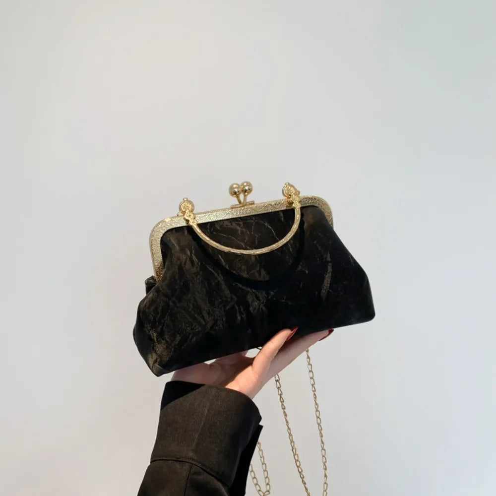 Una mano sostiene un bolso de mano de terciopelo negro con ribetes y lazo dorado contra un fondo claro.