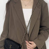 A woman models a brown blazer and white top, featuring a black bag with a gold chain strap.