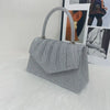 A silver glitter textured handbag with a handle is displayed in front of a photo backdrop.