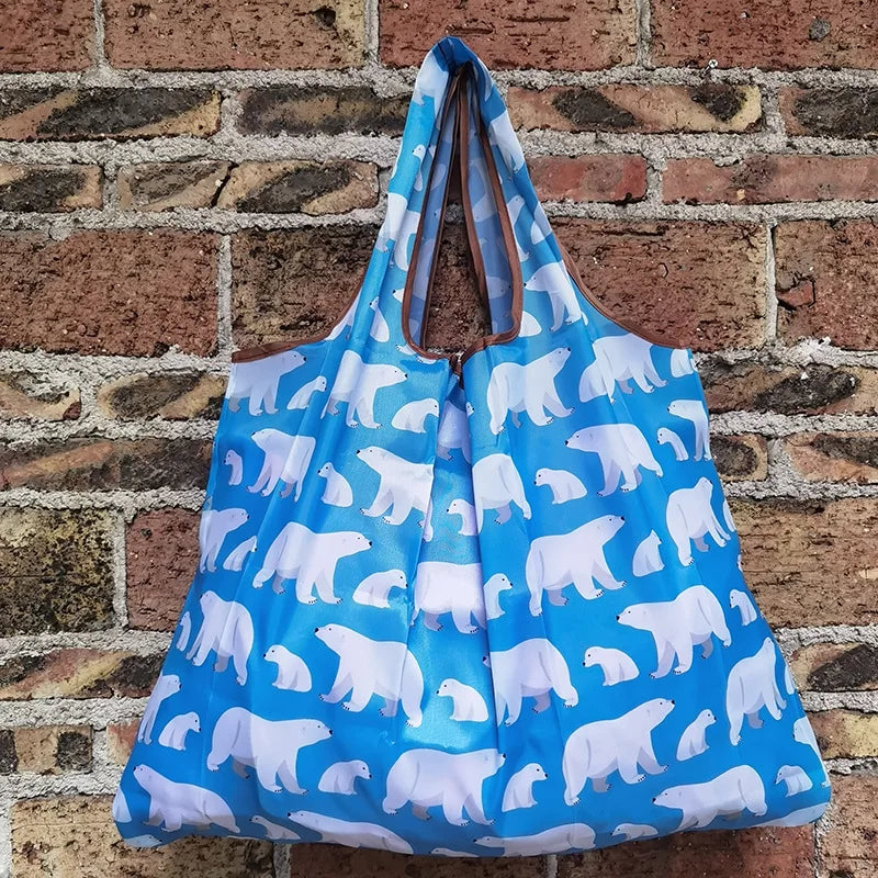 A light blue reusable shopping bag featuring a white polar bear print, displayed against a brick wall.
