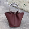 Ein tiefburgunderes Leder-Bucket-Bag mit einem hellgrauen Stoffgriff auf einer Betonoberfläche.