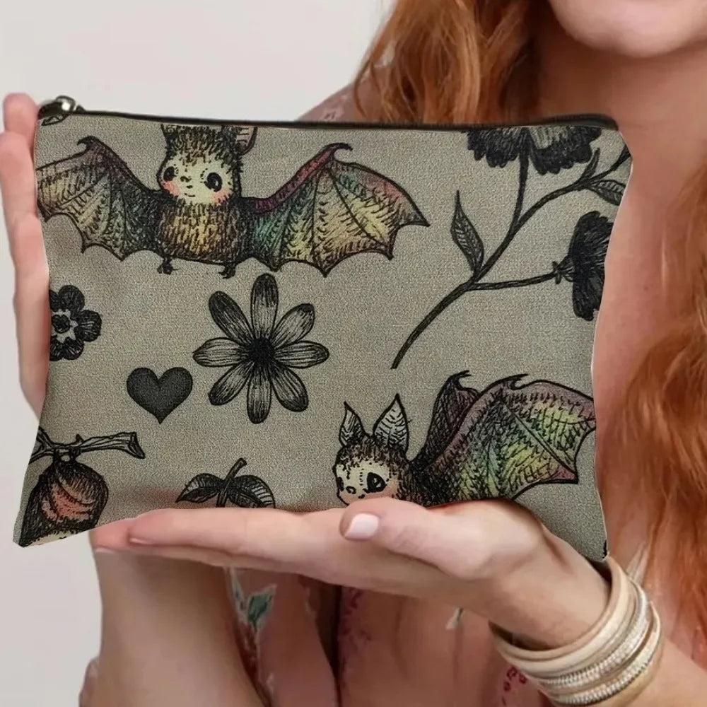 Una mano sostiene una bolsa de almacenamiento con cremallera de lona con un diseño de murciélago sobre un fondo gris.