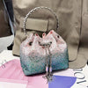 A pink and blue crystal-embellished evening clutch with a silver chain resting on a pink surface.
