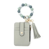 A light gray leather card holder with a beaded tassel keychain attached.