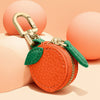 Orange leather coin purse keychain with a brass clasp and green fabric detail, resting on a peach-colored surface.