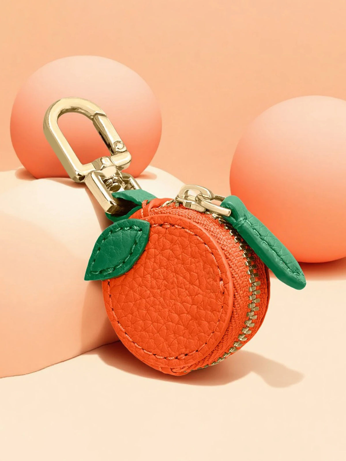 Orange leather coin purse keychain with a brass clasp and green fabric detail, resting on a peach-colored surface.