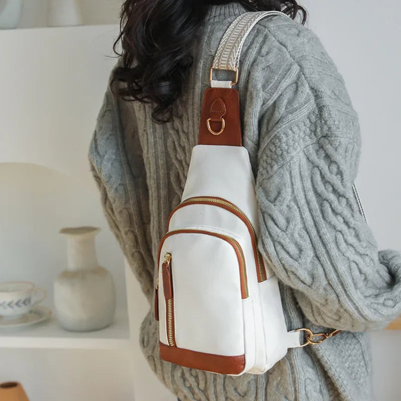 A woman is holding a beige and white PU leather crossbody sling bag with a brown strap over her sweater.