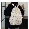 A white corduroy fashion backpack with a pattern of red cherries is worn by a person.