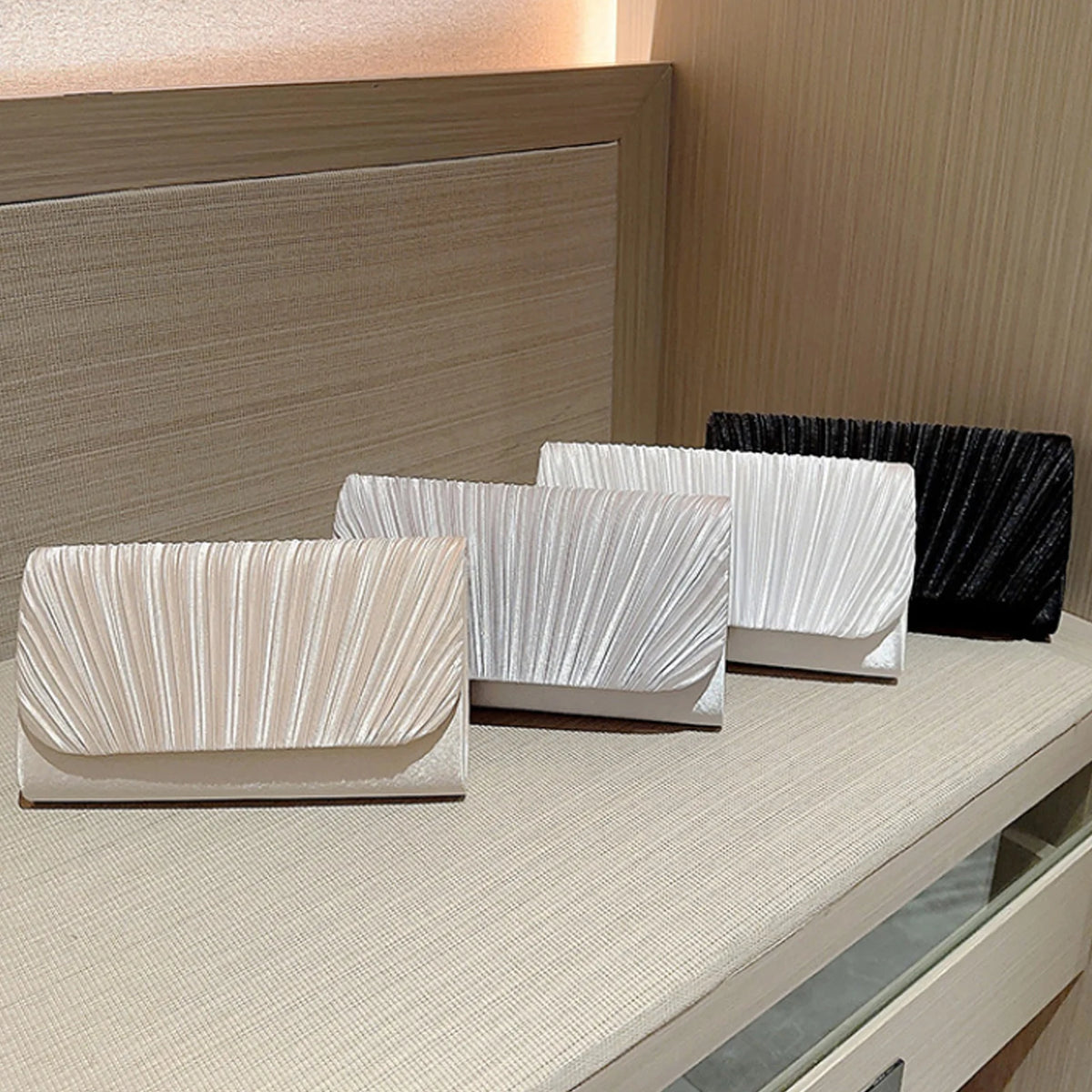 A display of several white and beige luxury chain shoulder clutch bags on a light-colored surface.