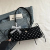Schwarze Schultertasche mit weißen Polka Dots und schwarzem Lederriemen auf einem Jeanshemd.