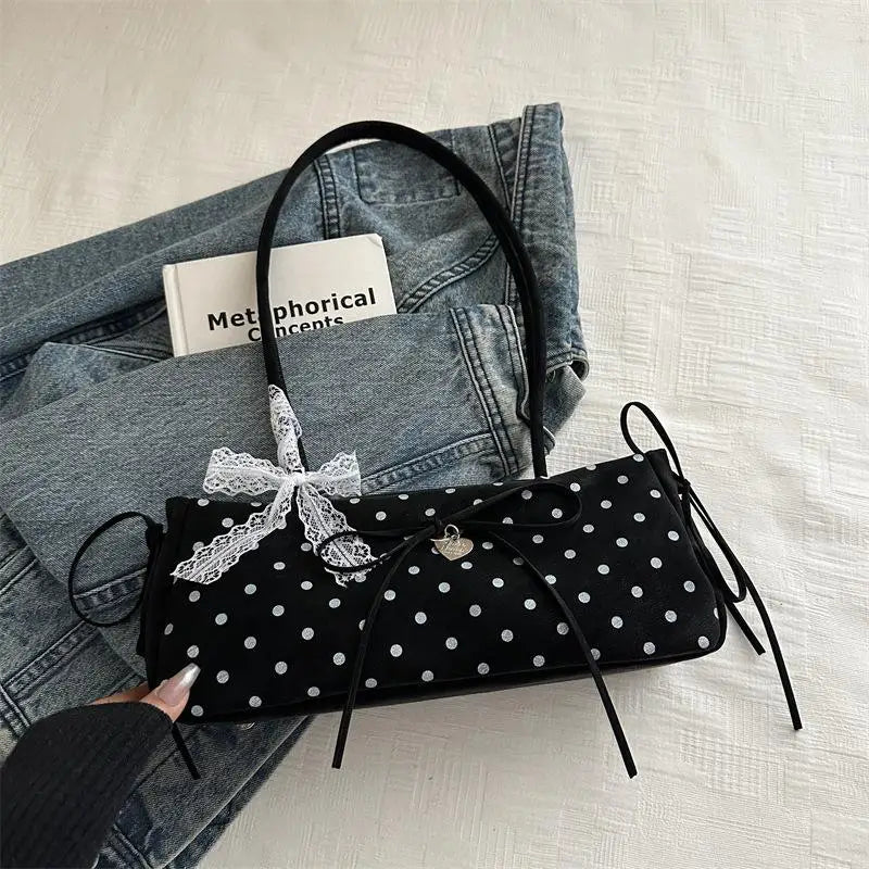 Schwarze Schultertasche mit weißen Polka Dots und schwarzem Lederriemen auf einem Jeanshemd.