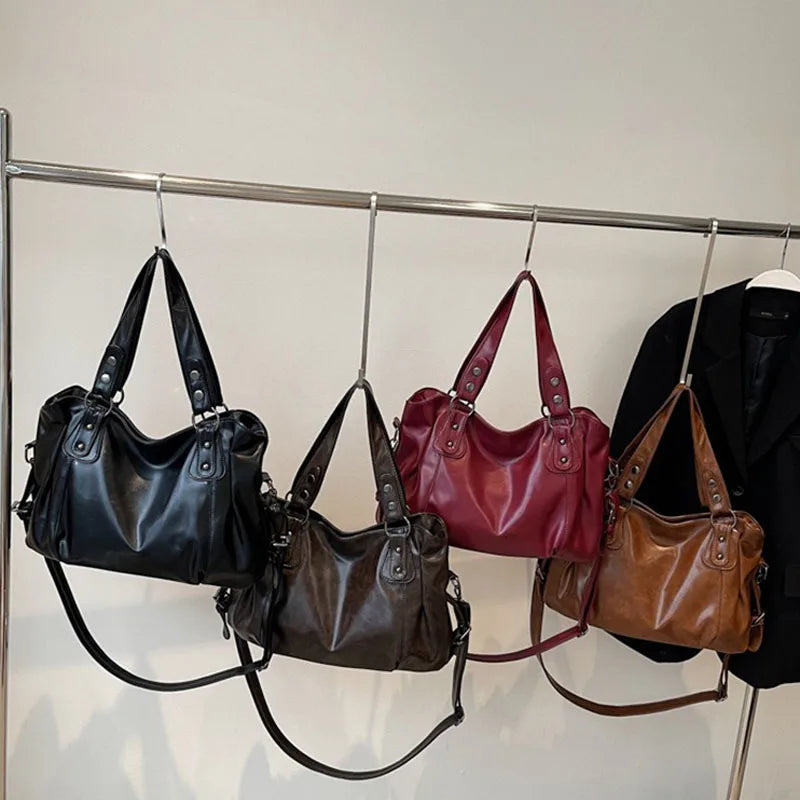 A display of four leather shoulder bags in black, burgundy, brown, and tan hanging on a metal rack.