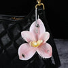 A pink orchid flower keychain is attached to a black quilted leather bag.