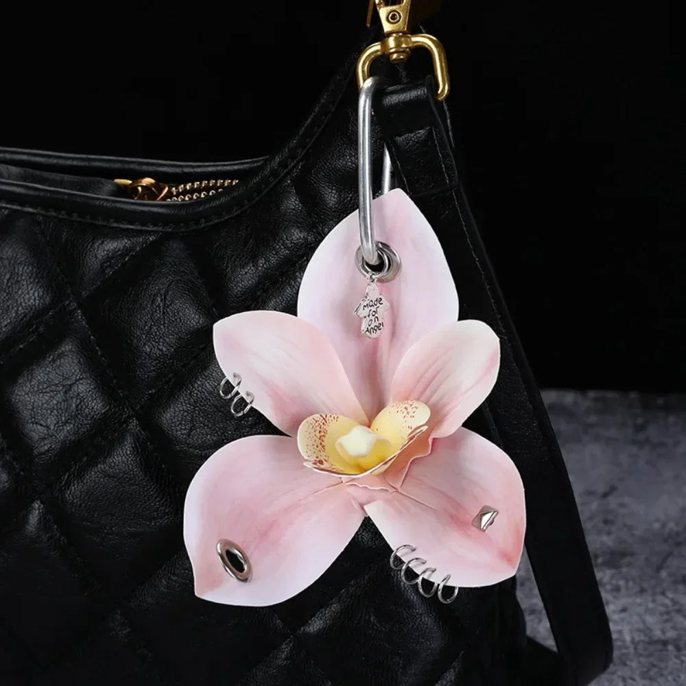 A pink orchid flower keychain is attached to a black quilted leather bag.