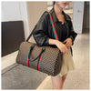 A woman is holding a brown plaid travel duffle bag and wearing a black leather jacket.