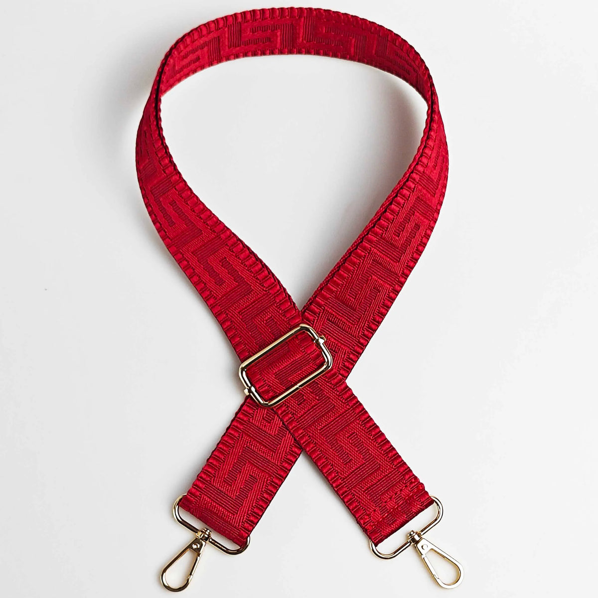 A red adjustable crossbody bag strap featuring a maze pattern and gold-toned hardware.
