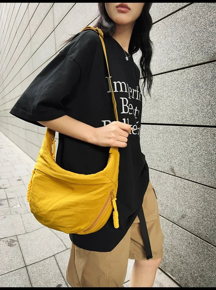 A woman wearing a black t-shirt and khaki shorts holds a yellow soft nylon crossbody bag.