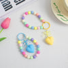 A colorful bead necklace featuring pink, blue, and green beads with a heart charm and gold O-ring clip.