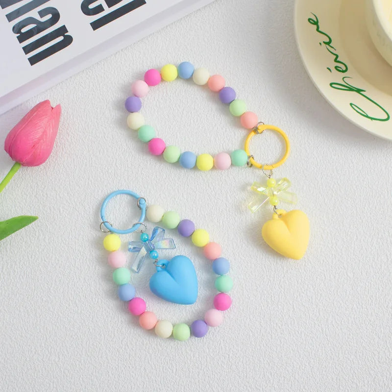 A colorful bead necklace featuring pink, blue, and green beads with a heart charm and gold O-ring clip.