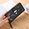 Clutch cartera de cuero PU negro con estampado de hoja grabada, sostenida por una mano sobre una superficie de madera.