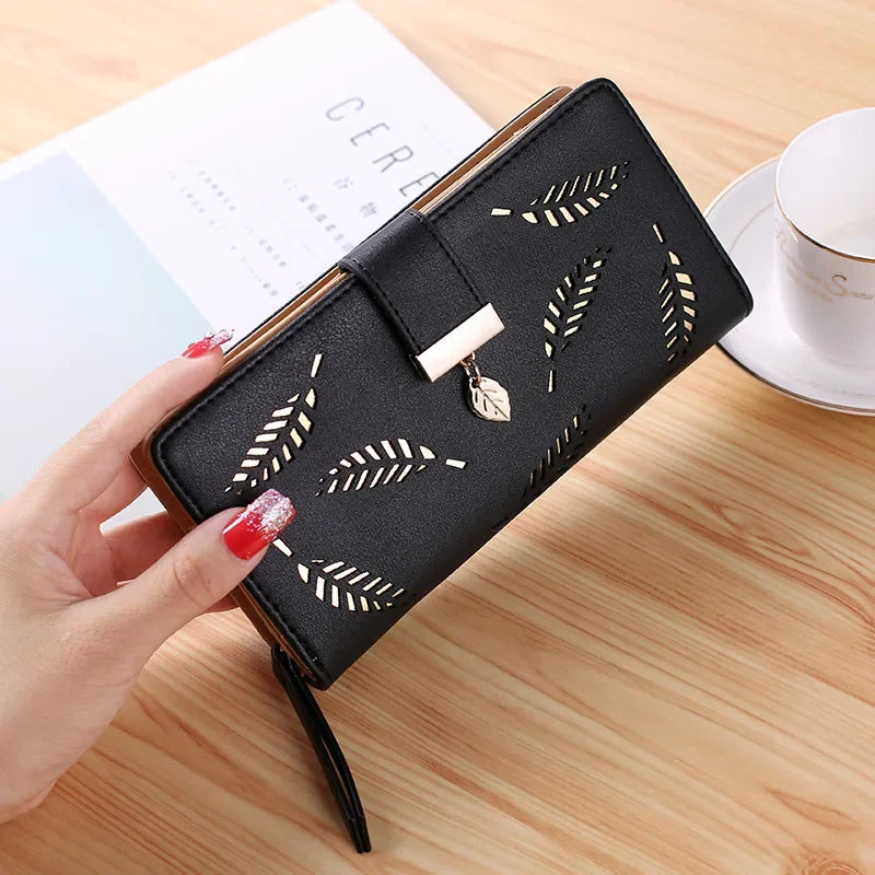 Clutch cartera de cuero PU negro con estampado de hoja grabada, sostenida por una mano sobre una superficie de madera.
