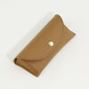 A tan PU leather hard shell sunglasses case lying on a white surface.
