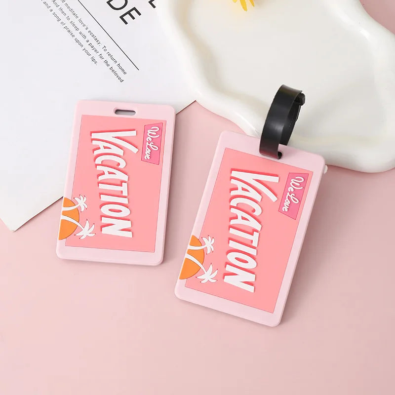 Two pink silicone letter luggage tags with white text and floral designs are displayed on a light surface.