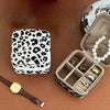 A leopard print PU leather jewelry storage box is shown open with rings and a pearl necklace inside, next to a watch.