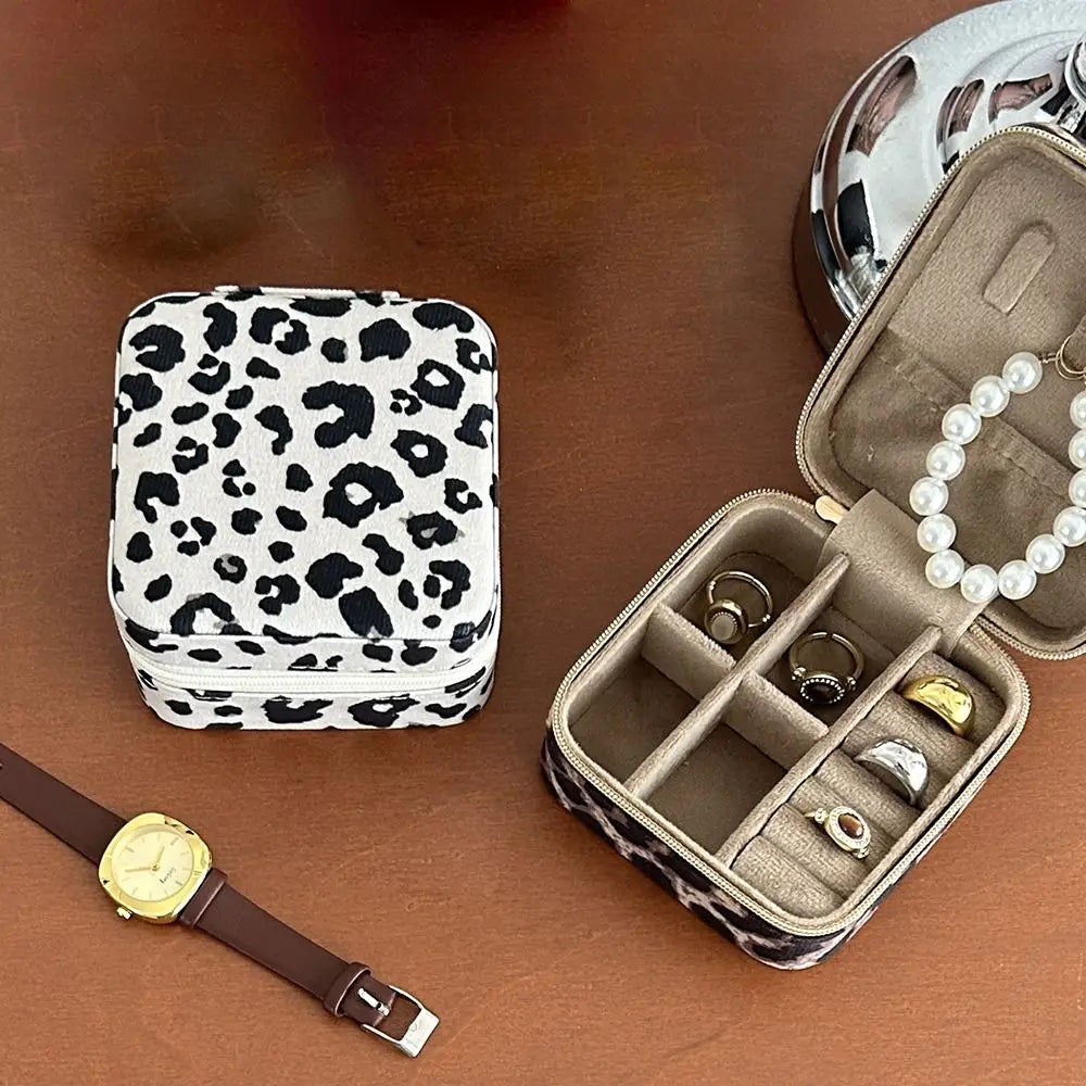 A leopard print PU leather jewelry storage box is shown open with rings and a pearl necklace inside, next to a watch.