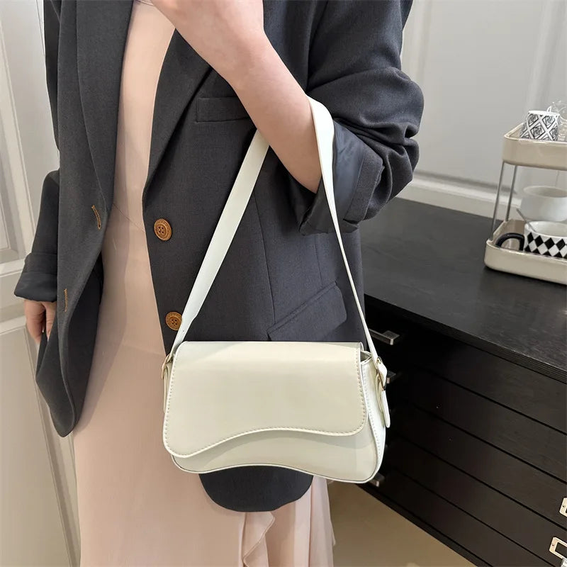 A woman holds a cream colored vintage curved flap shoulder bag with a white strap against a dark cabinet.