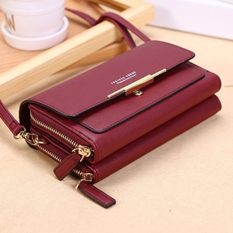 A maroon women's multi-card shoulder wallet with gold hardware is shown lying on a light brown surface.