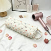 A pink hairdryer storage bag with a quilted pattern rests on a white cloth next to a pink hair dryer.