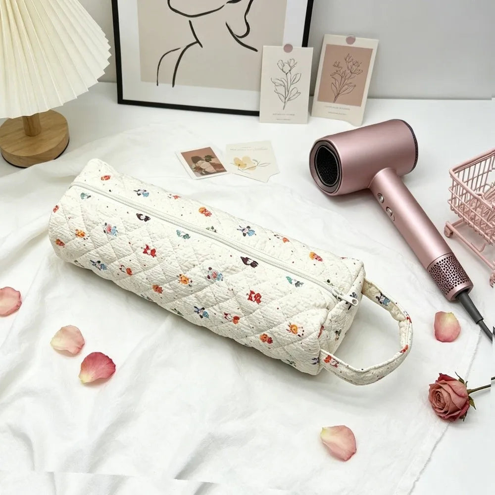 A pink hairdryer storage bag with a quilted pattern rests on a white cloth next to a pink hair dryer.