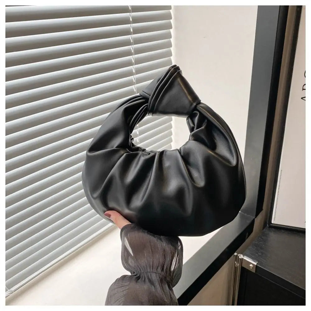 Un bolso de mano negro con lazo de cuero, mostrado contra una persiana de ventana.