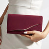 A deep burgundy velvet evening clutch held by a person against a white dress.