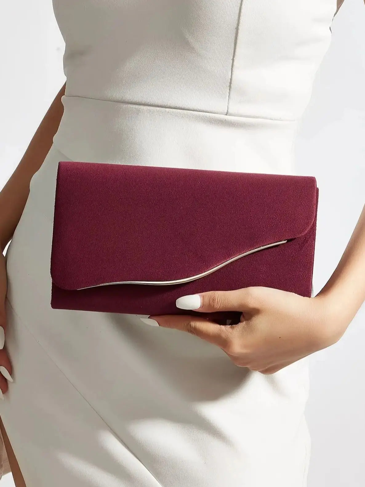 A deep burgundy velvet evening clutch held by a person against a white dress.