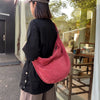 A person wearing a black shirt and light pants holds a pink corduroy casual crossbody bag in front of a glass door.